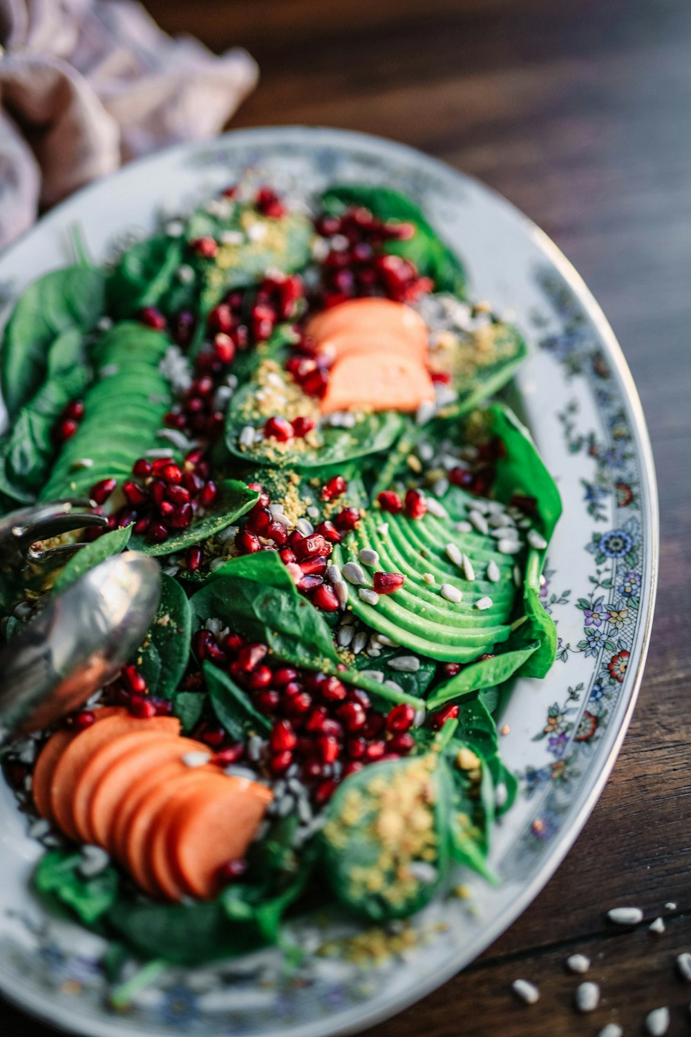 Platter of leafy greens, avocado, carrots, and pomegranate seeds