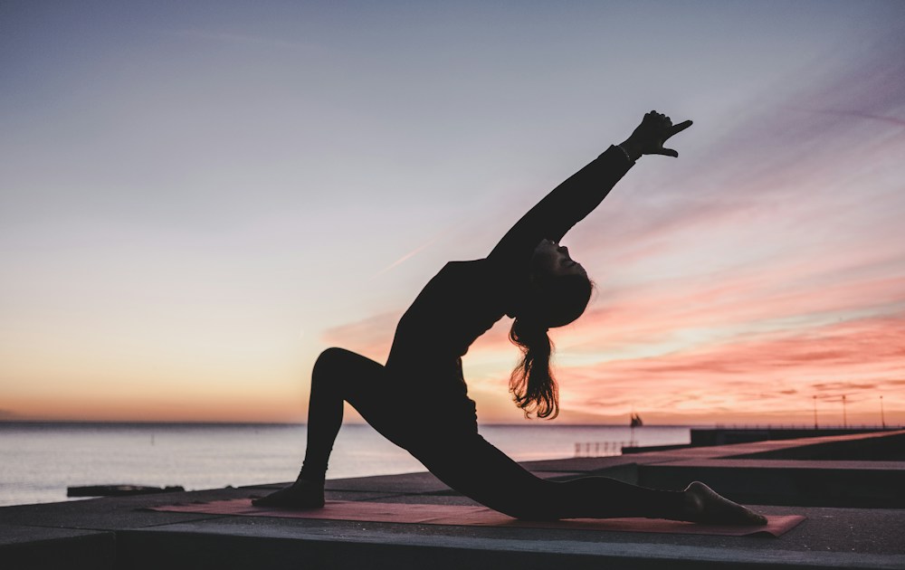 Woman practicing a yoga stretch beside the water at sunset